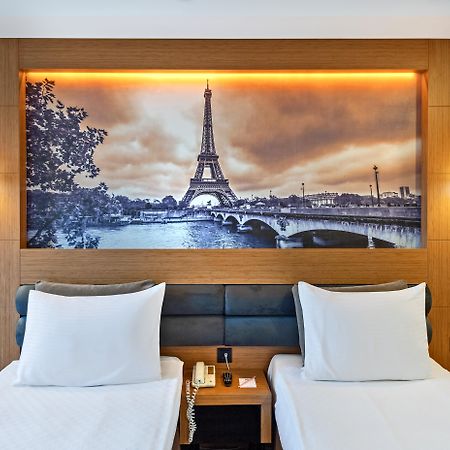 Sealife Family Resort Hotel Antalya Exterior foto The photo depicts a hotel room featuring two single beds with white bedding. Behind the beds, there's a large mural of the Eiffel Tower, set against a scenic backdrop of the Seine River. The image has a vintage, sepia-toned appearance, enhancing the 