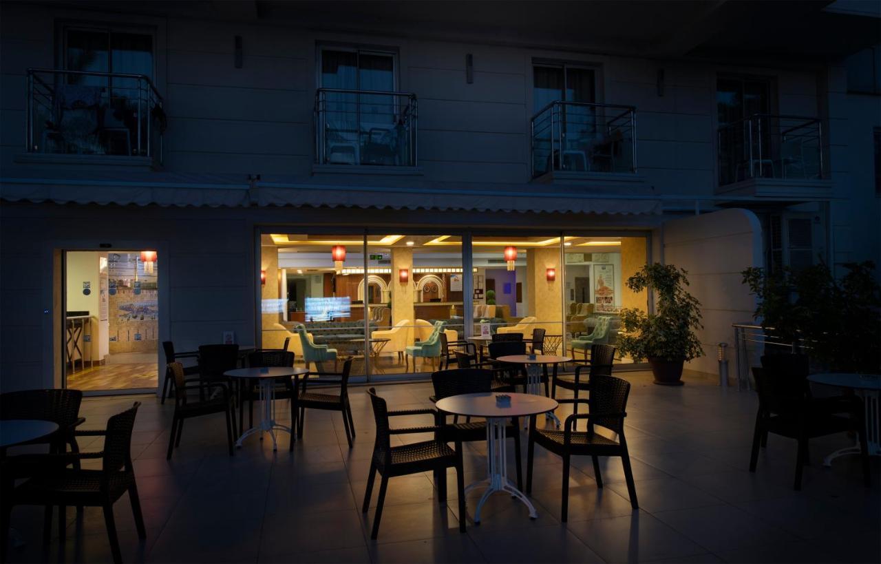 Sealife Family Resort Hotel Antalya Exterior foto The photo depicts an outdoor seating area of a café or restaurant. In the foreground, there are several black chairs and a small round table. In the background, through large windows, you can see the interior of the establishment, which is warmly lit