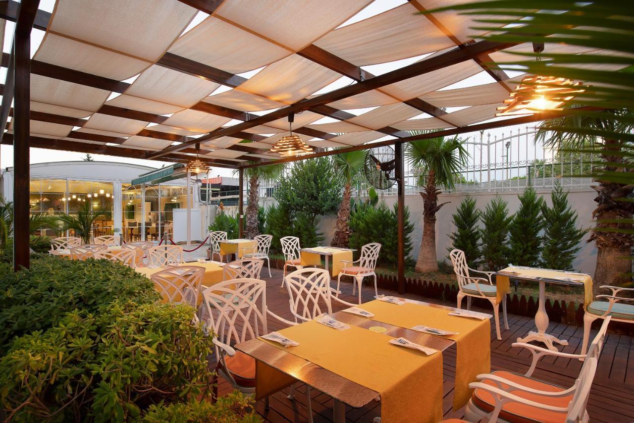 Sealife Family Resort Hotel Antalya Exterior foto The photo depicts an outdoor dining area of a restaurant featuring a pergola with fabric coverings that provide shade. The space is arranged with several tables adorned with bright yellow tablecloths. The chairs are designed with a distinctive white 