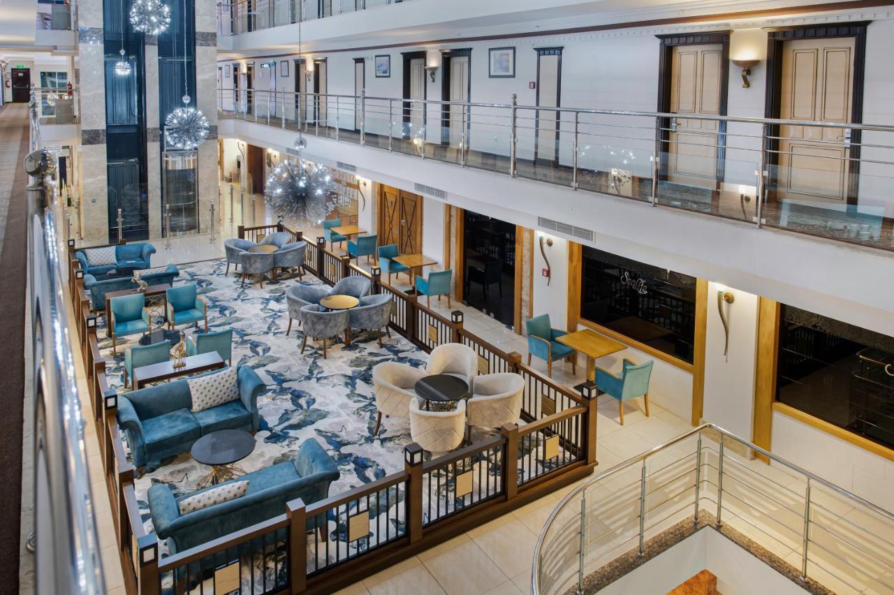 Sealife Family Resort Hotel Antalya Exterior foto The photo shows the interior of a modern hotel lobby or lounge area. There are multiple seating arrangements with stylish teal chairs and cream-colored sofas set around tables. The floor features a large, decorative rug, and the walls have elegant fi