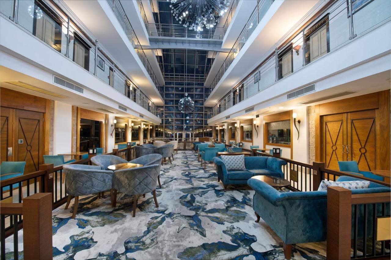Sealife Family Resort Hotel Antalya Exterior foto The photo shows a spacious and elegantly designed hotel lobby. There are two levels with balconies overlooking the main area. The lobby features plush, stylish seating arranged around small tables. The floor is decorated with a colorful, abstract car