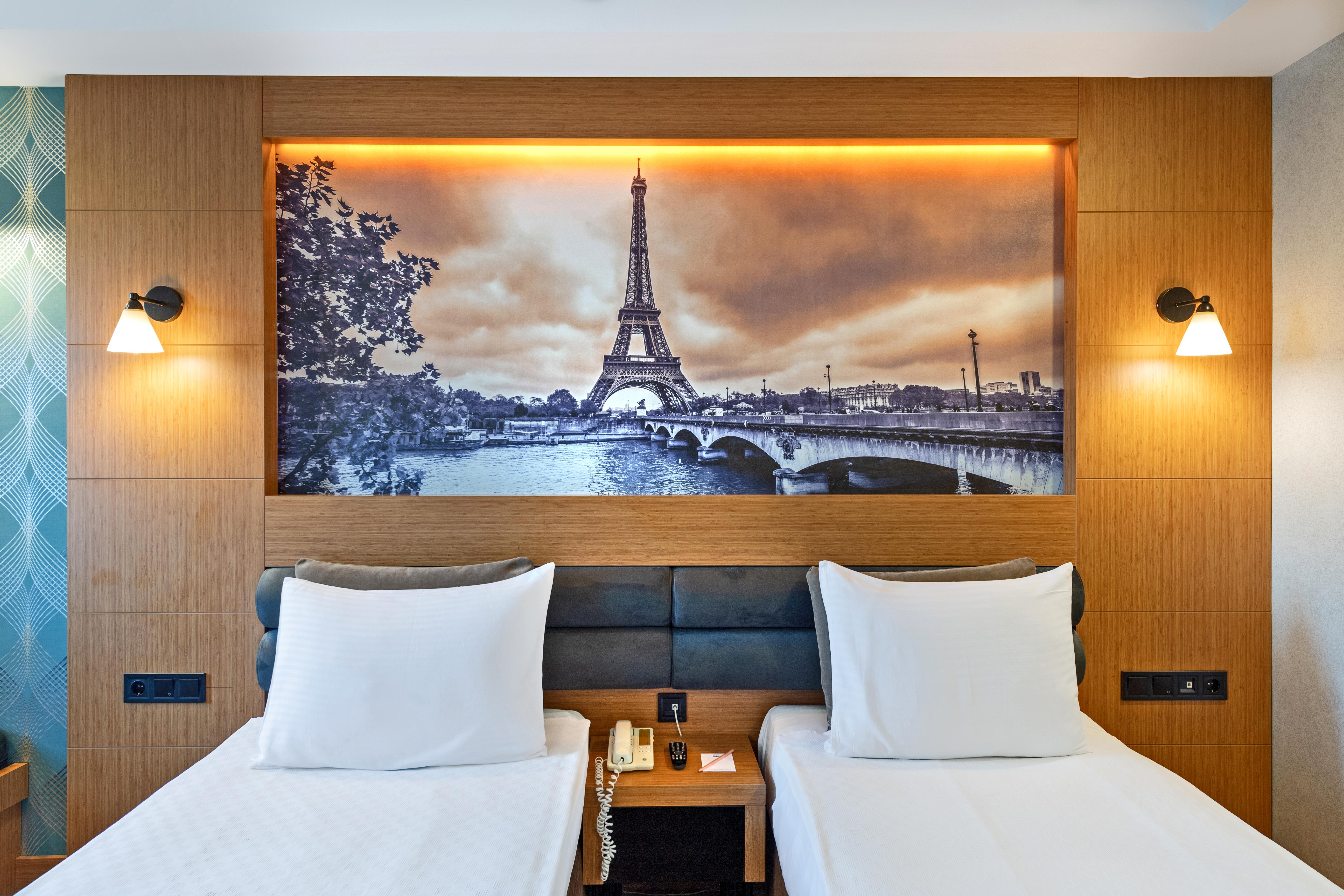 Sealife Family Resort Hotel Antalya Exterior foto The photo depicts a hotel room featuring two single beds with white bedding. Behind the beds, there's a large mural of the Eiffel Tower, set against a scenic backdrop of the Seine River. The image has a vintage, sepia-toned appearance, enhancing the 