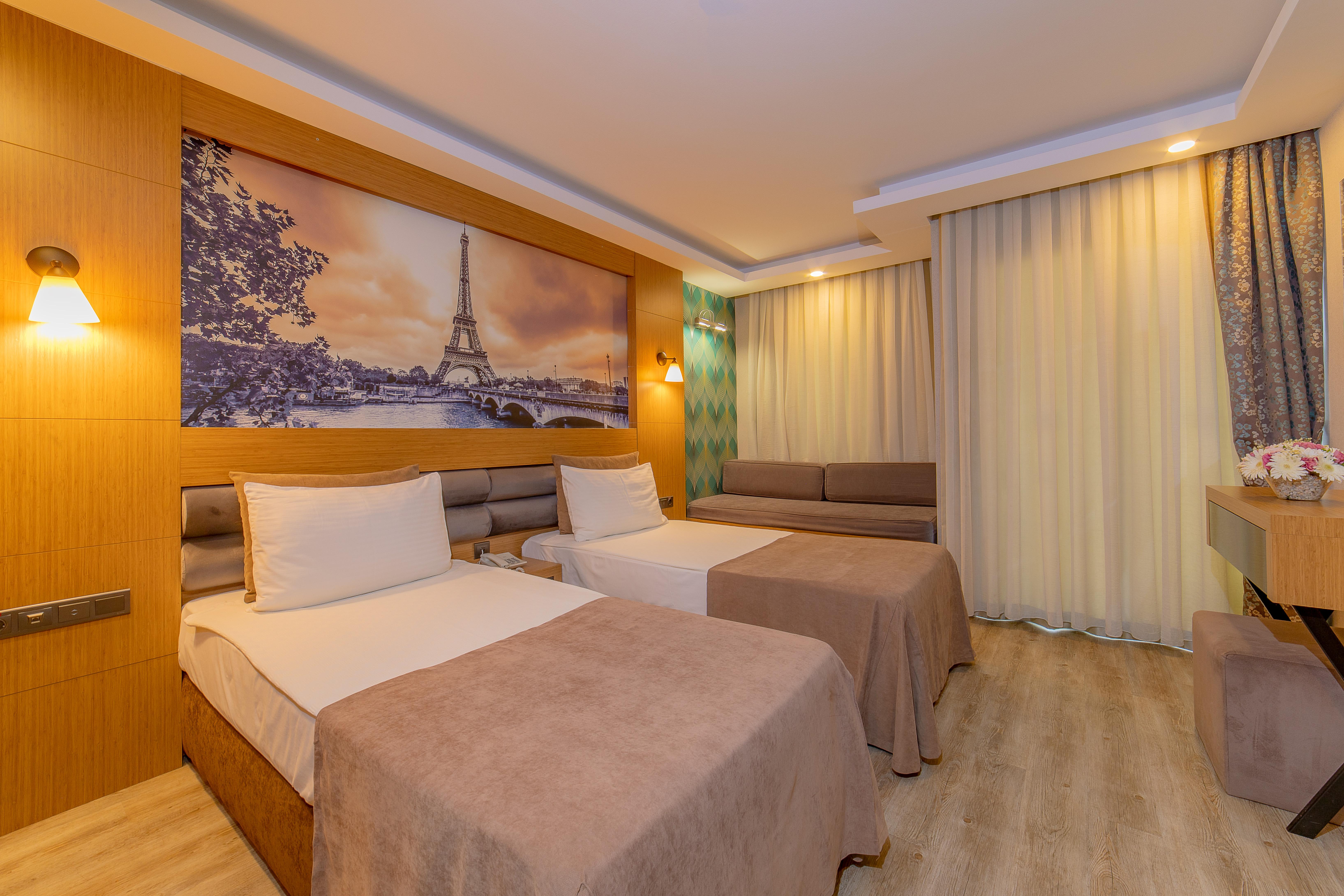 Sealife Family Resort Hotel Antalya Exterior foto The photo shows a modern hotel room featuring two beds with beige bedspreads. There is a large wall mural depicting a scenic view of the Eiffel Tower in Paris. The room is well-lit, with soft lighting fixtures on the walls. To the right, there is a s