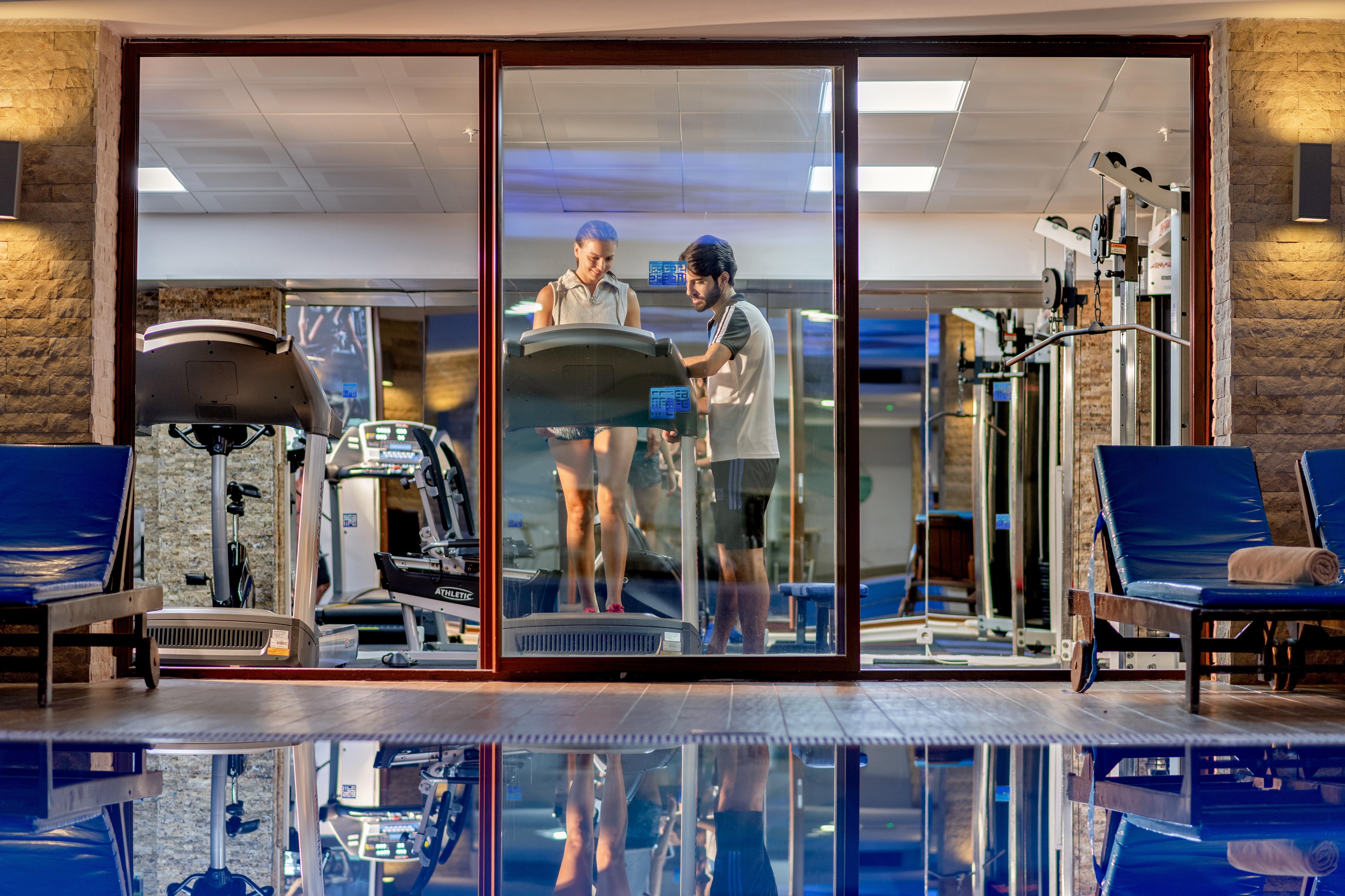 Sealife Family Resort Hotel Antalya Exterior foto The photo shows a modern gym area viewed through a large glass window. Inside the gym, there are two individuals, one on a treadmill and the other standing beside it, possibly offering guidance or support. The gym is well-equipped, featuring various 