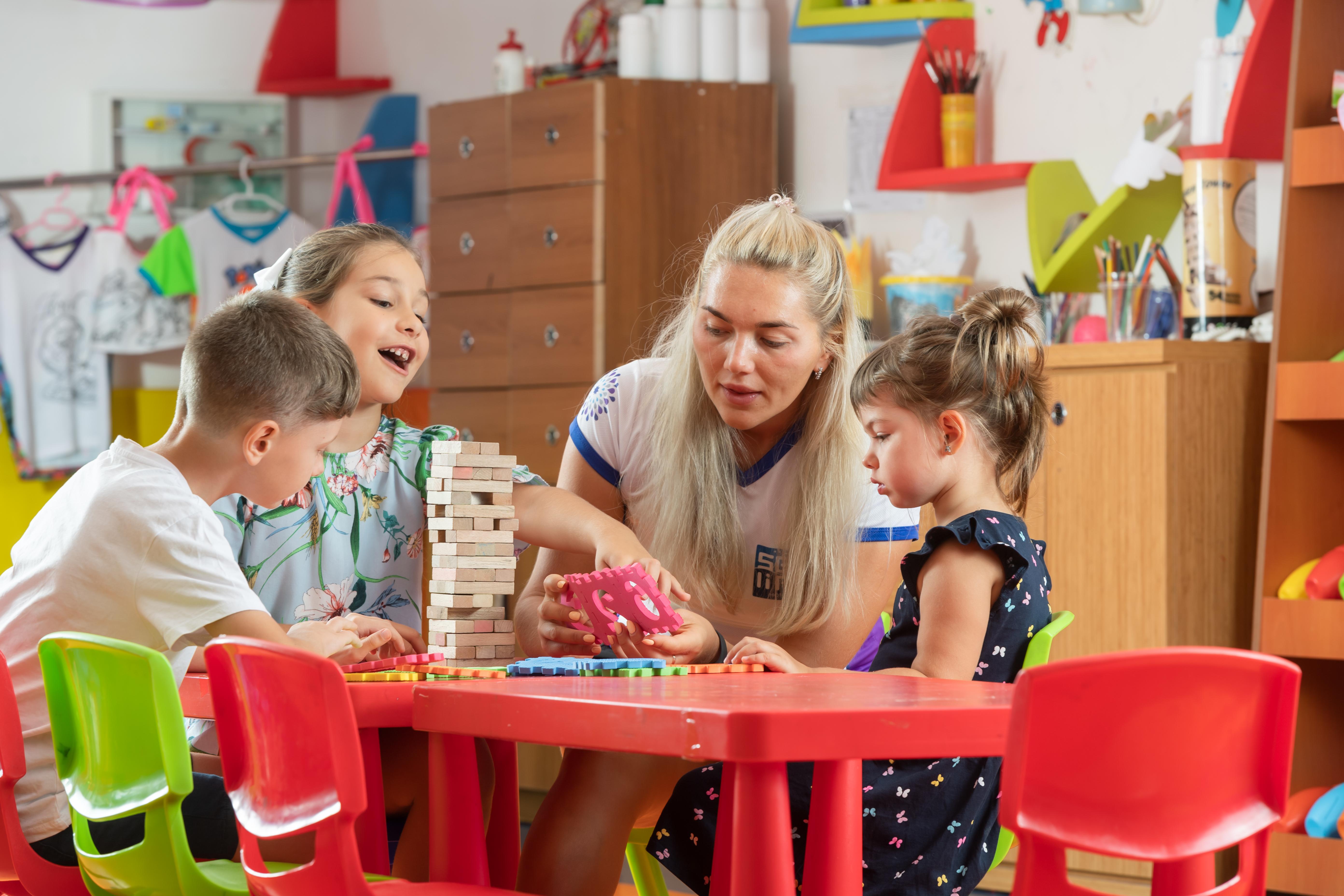 Sealife Family Resort Hotel Antalya Exterior foto The photo depicts a playful and engaging scene in a classroom or activity space. There are four children sitting at a bright red table, focused on a game. Two girls, one wearing a colorful floral shirt and the other in a dark dress with ruffles, are 
