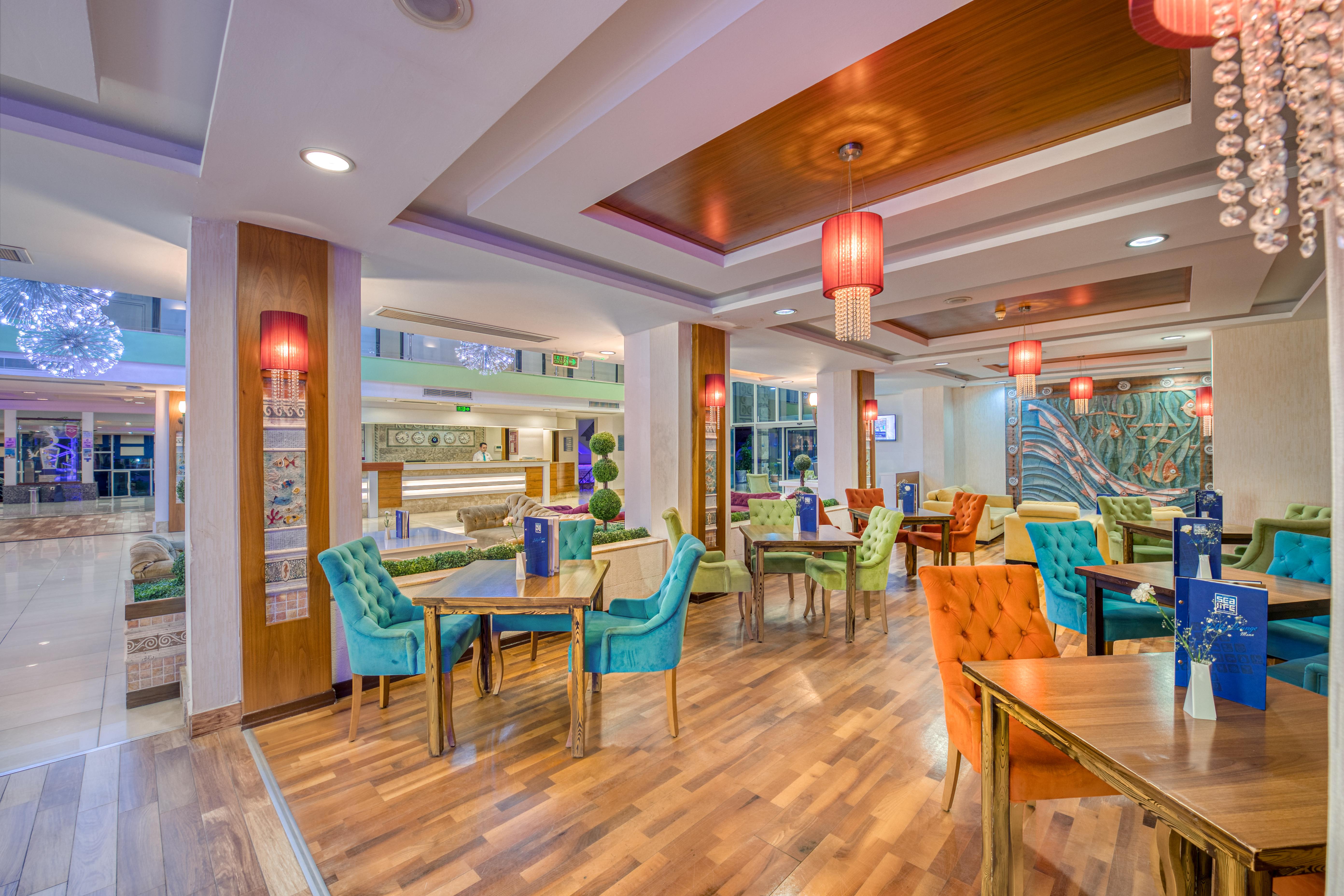 Sealife Family Resort Hotel Antalya Exterior foto The photo depicts a vibrant and modern restaurant interior. The space features multiple dining tables, each adorned with blue menus. The chairs are brightly colored, in shades of teal, orange, and other hues, adding a playful touch to the decor. The 