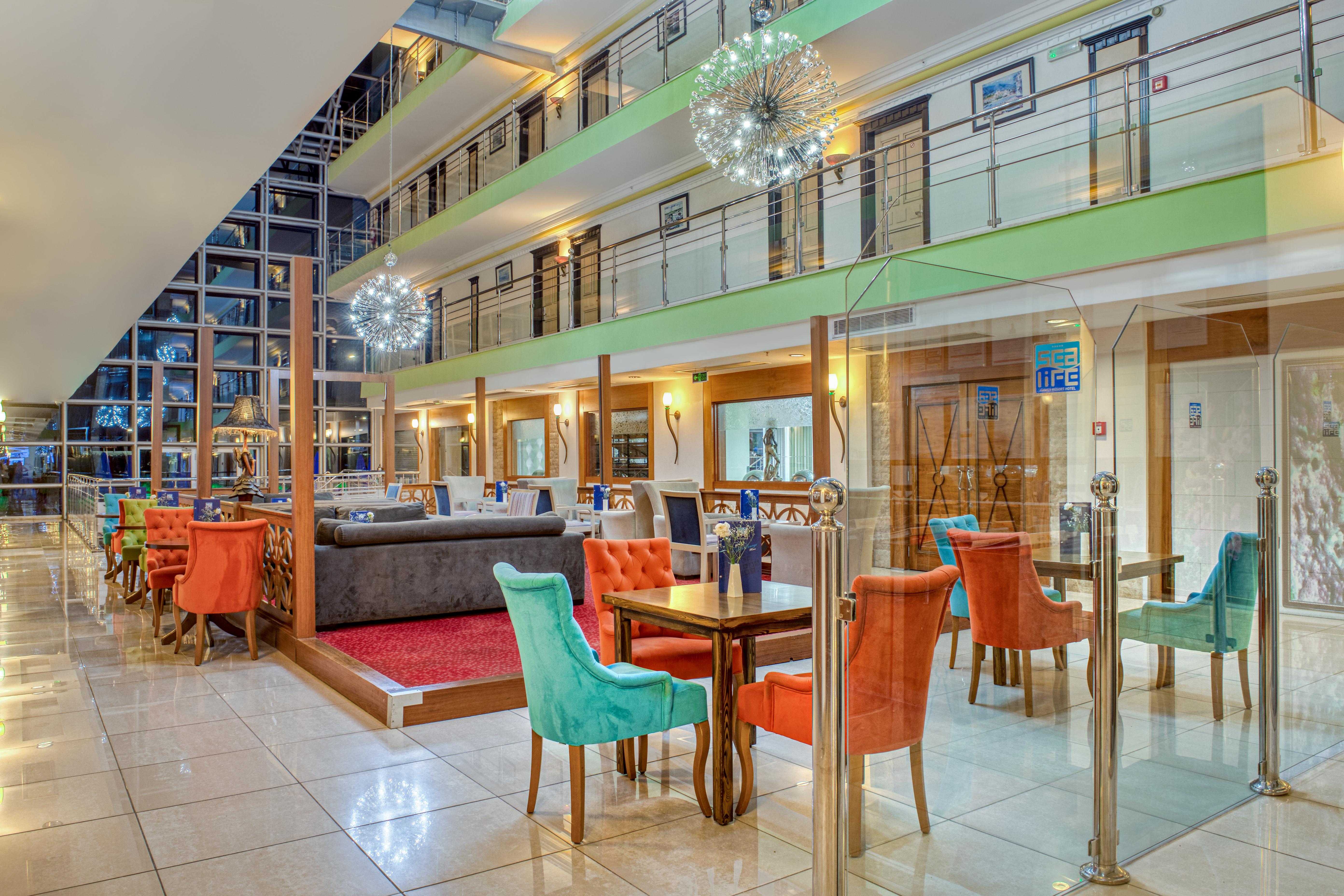 Sealife Family Resort Hotel Antalya Exterior foto The photo shows the interior of a modern hotel lobby or dining area. It features a spacious room with multiple levels visible. The decor includes colorful chairs in orange and turquoise, along with wooden tables. 

There are glass barriers separating