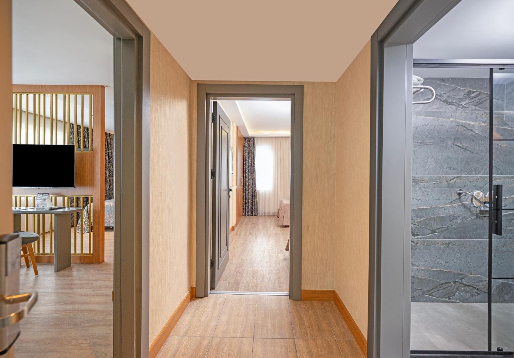 Sealife Family Resort Hotel Antalya Cameră foto The image shows a hallway with a few separate rooms visible. On the left side, there's a view of a modern living area with a television and some furniture. At the end of the hallway, light is coming from a window in another room, indicating it may be