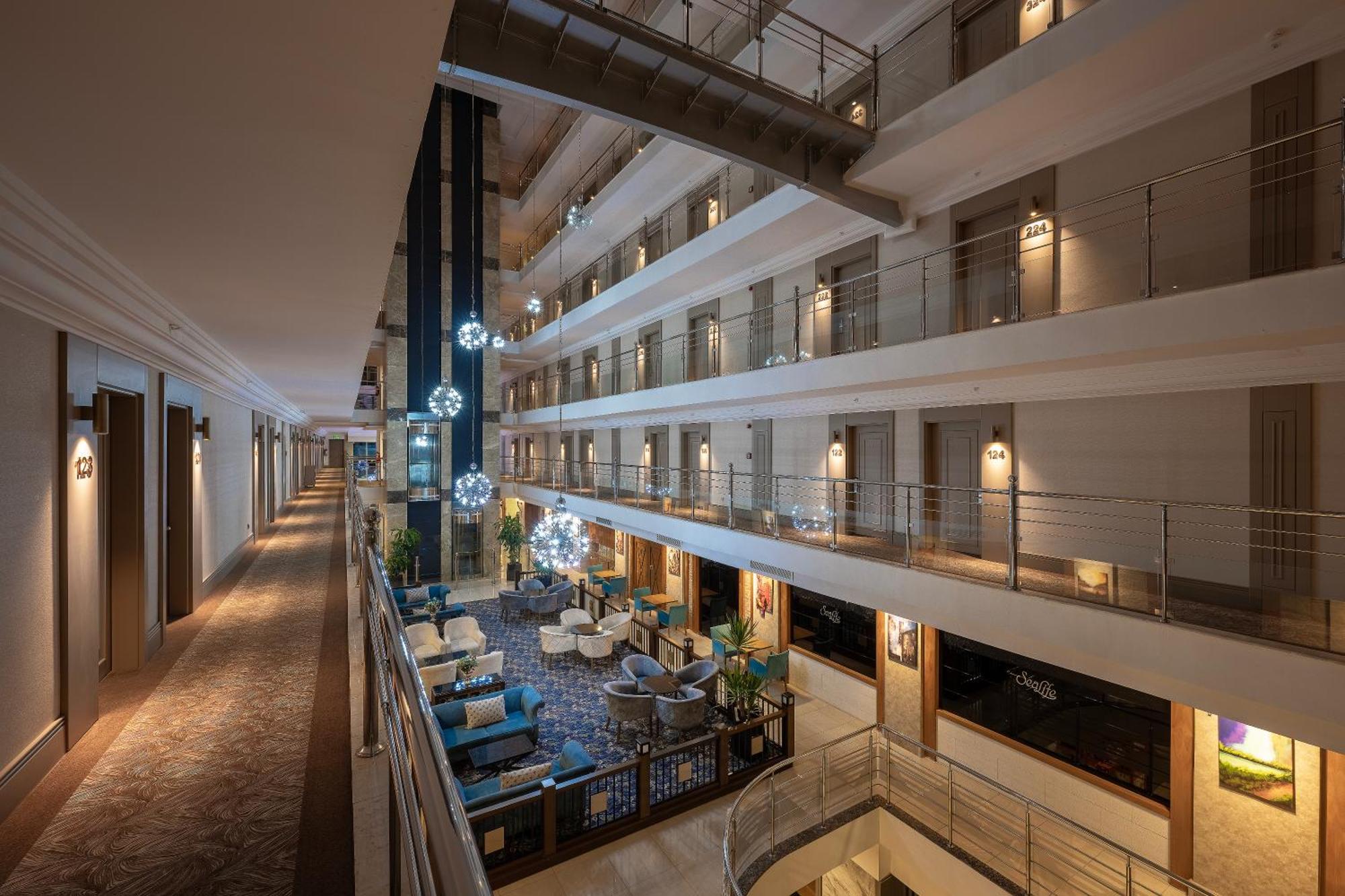 Sealife Family Resort Hotel Antalya Exterior foto The photo shows the interior of a modern hotel. It features multiple floors with open balconies overlooking a central atrium. The atrium is well-lit and decorated with comfortable seating arrangements, including couches and chairs. Elegant lighting f