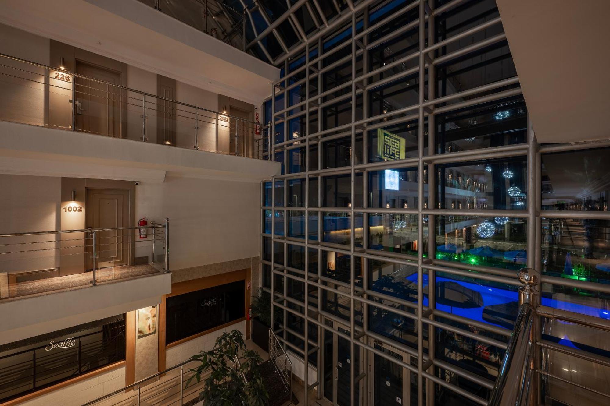 Sealife Family Resort Hotel Antalya Exterior foto The photo shows an interior view of a modern building at night. There's a glass façade that allows for a view of the outside, which appears to be illuminated with various lights. Inside, there are several levels with walkways and balconies. The desig