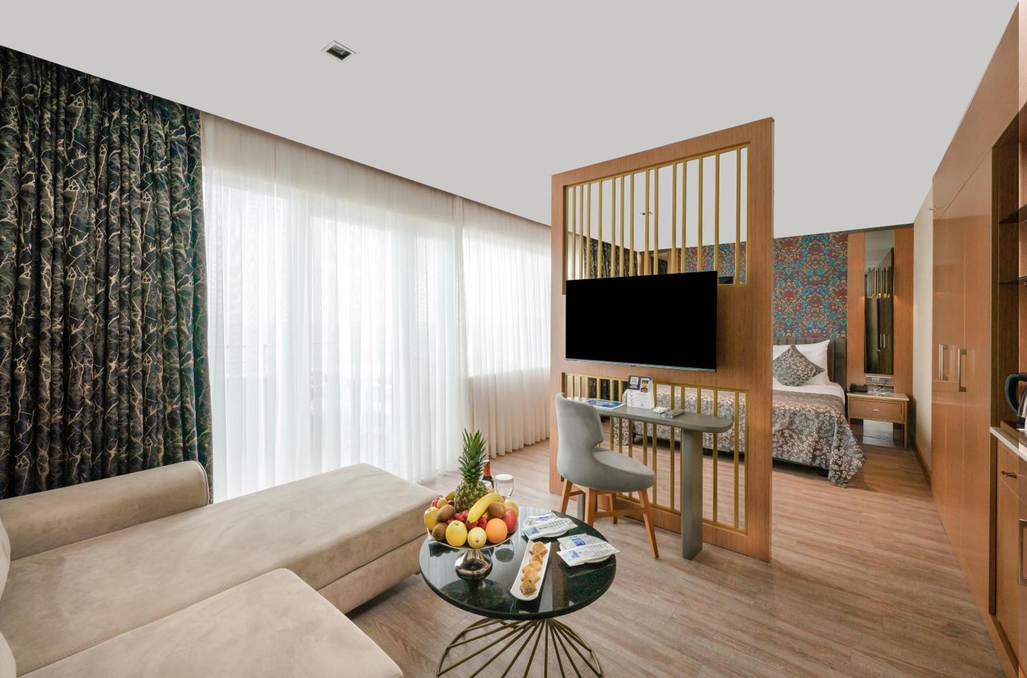 Sealife Family Resort Hotel Antalya Cameră foto The photo shows a modern hotel room that features a stylish and functional design. On one side, there is a comfortable light-colored sofa positioned next to a round coffee table adorned with a variety of fruits and snacks. The coffee table has a slee