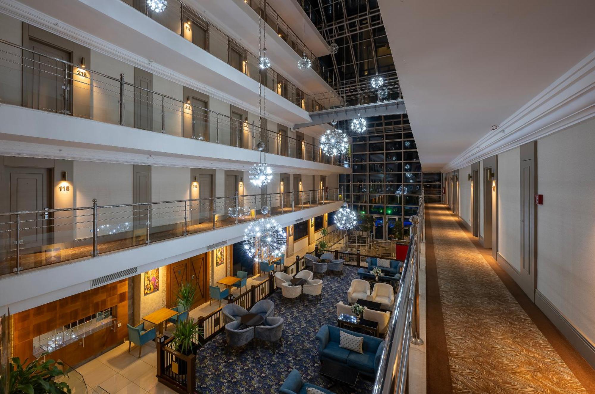 Sealife Family Resort Hotel Antalya Exterior foto The image shows the interior of a hotel lobby or atrium. It features multiple levels with balconies overlooking a central area. The design includes elegant lighting fixtures that resemble decorative spheres, hanging from the ceiling. The floor is ado