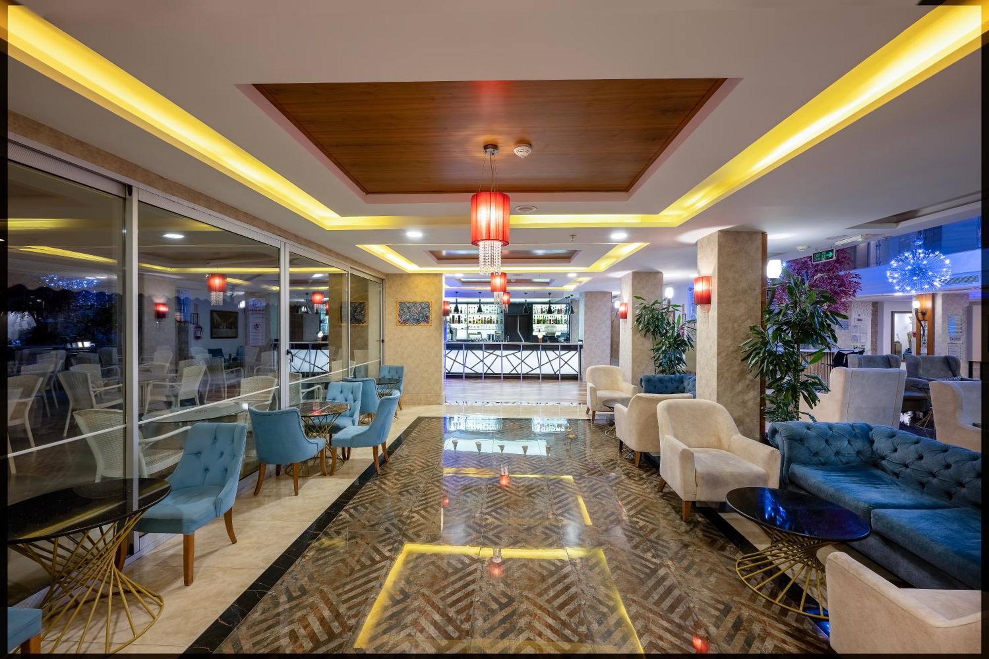 Sealife Family Resort Hotel Antalya Exterior foto The image shows a stylish interior of a lounge or hotel lobby. There are several comfortable seating areas with blue and white chairs. The floor is designed with a patterned tile that complements the modern decor. In the background, there is a bar ar